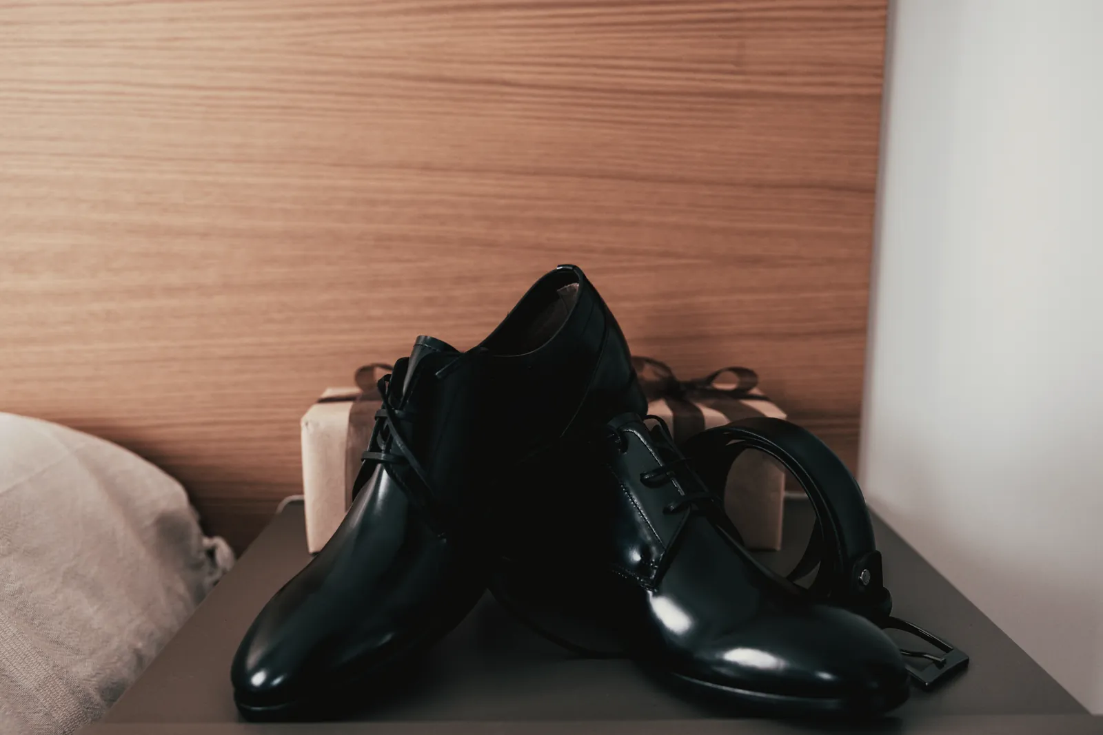 Le scarpe nere lucide e la cintura sul comodino di legno.