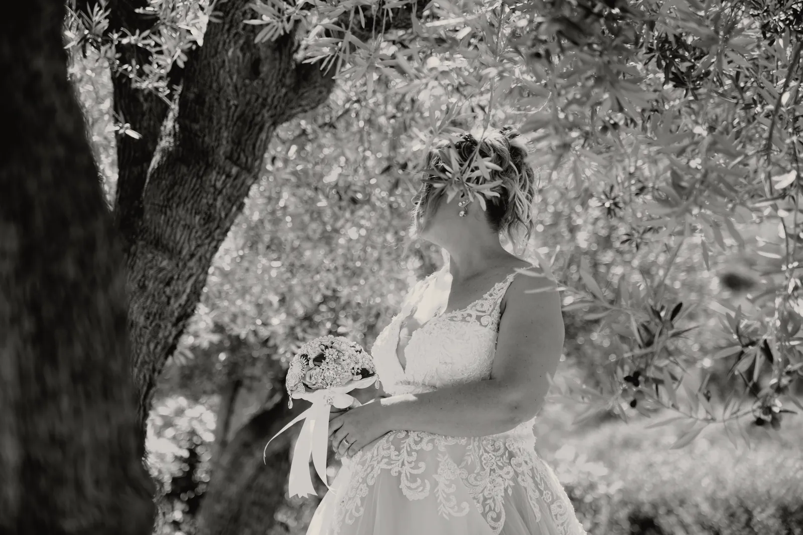 La sposa fra i rami d’ulivo, il viso in parte nascosto dalle foglie, il bouquet in mano.