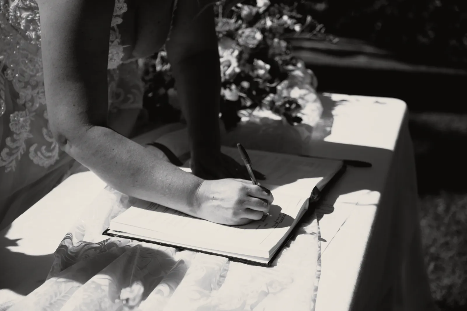 La mano della sposa firma il registro, fra il pizzo della tovaglia e i fiori.