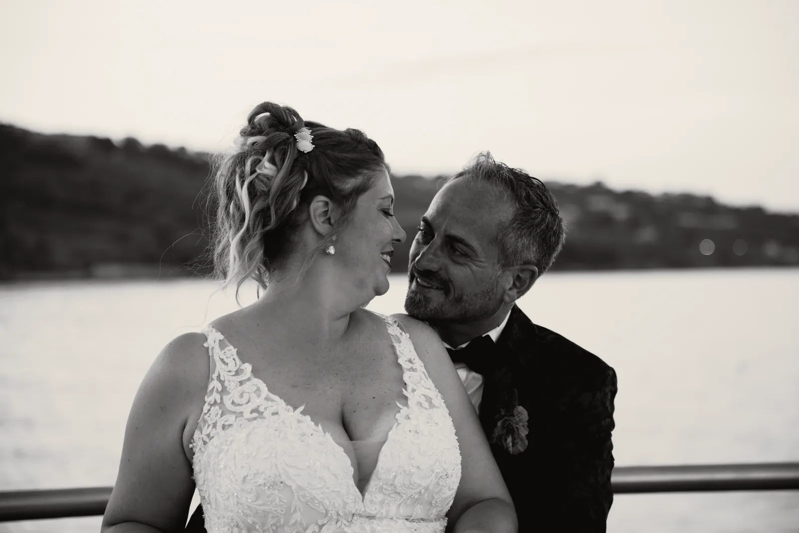 Sul pontile la sposa sorride a occhi bassi; lo sposo, la guancia contro la sua spalla, la guarda. Dietro, il golfo.