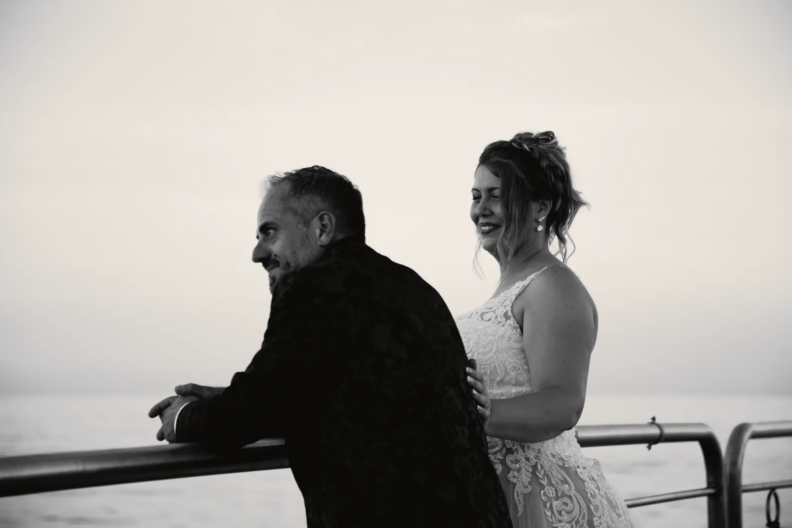Lo sposo appoggiato alla ringhiera si volta verso la sposa, che gli tiene una mano sulla spalla e ride.