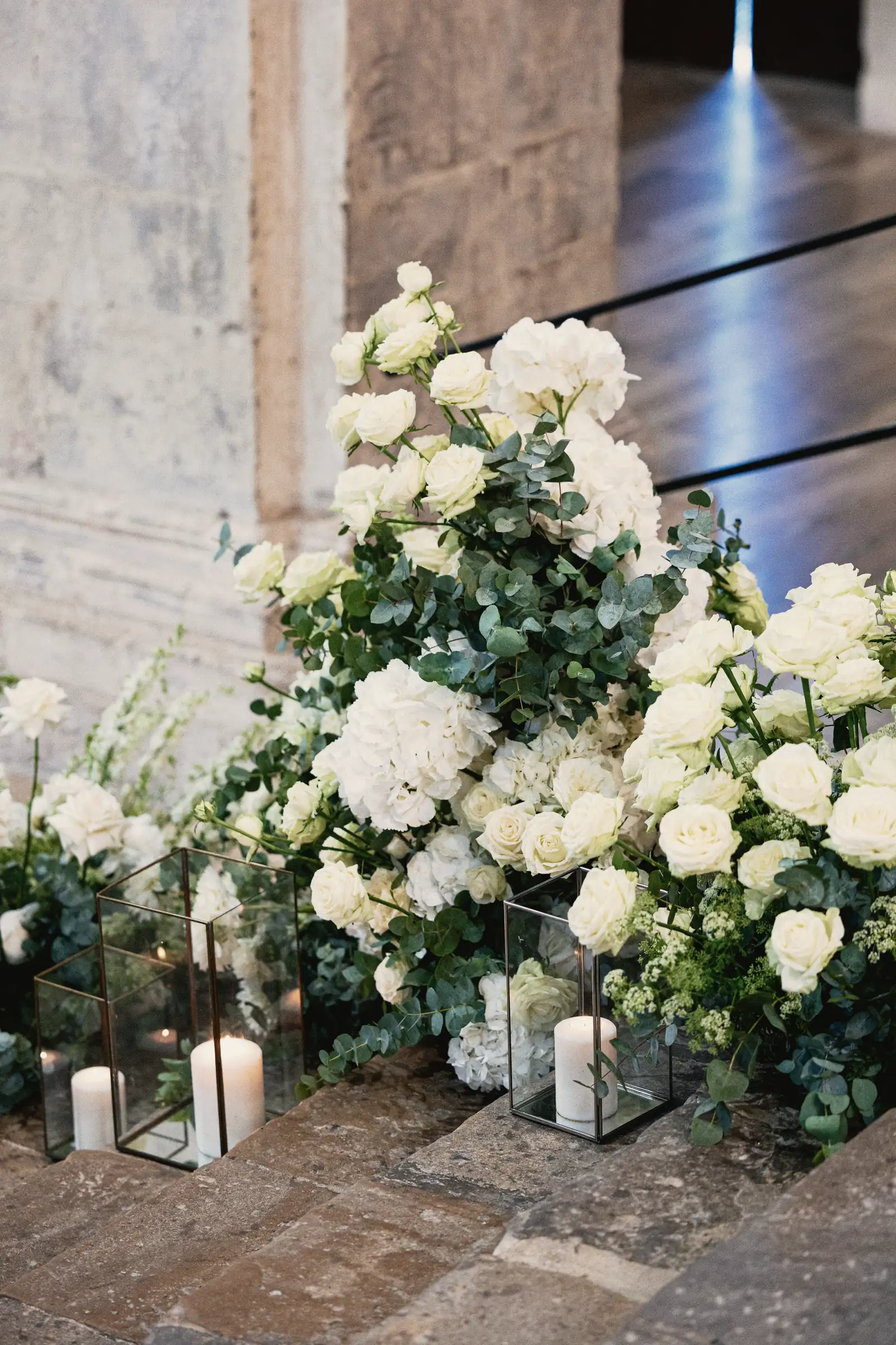 Rose bianche, ortensie e candele nelle lanterne di vetro, ai piedi di una colonna, prima che arrivi qualcuno.