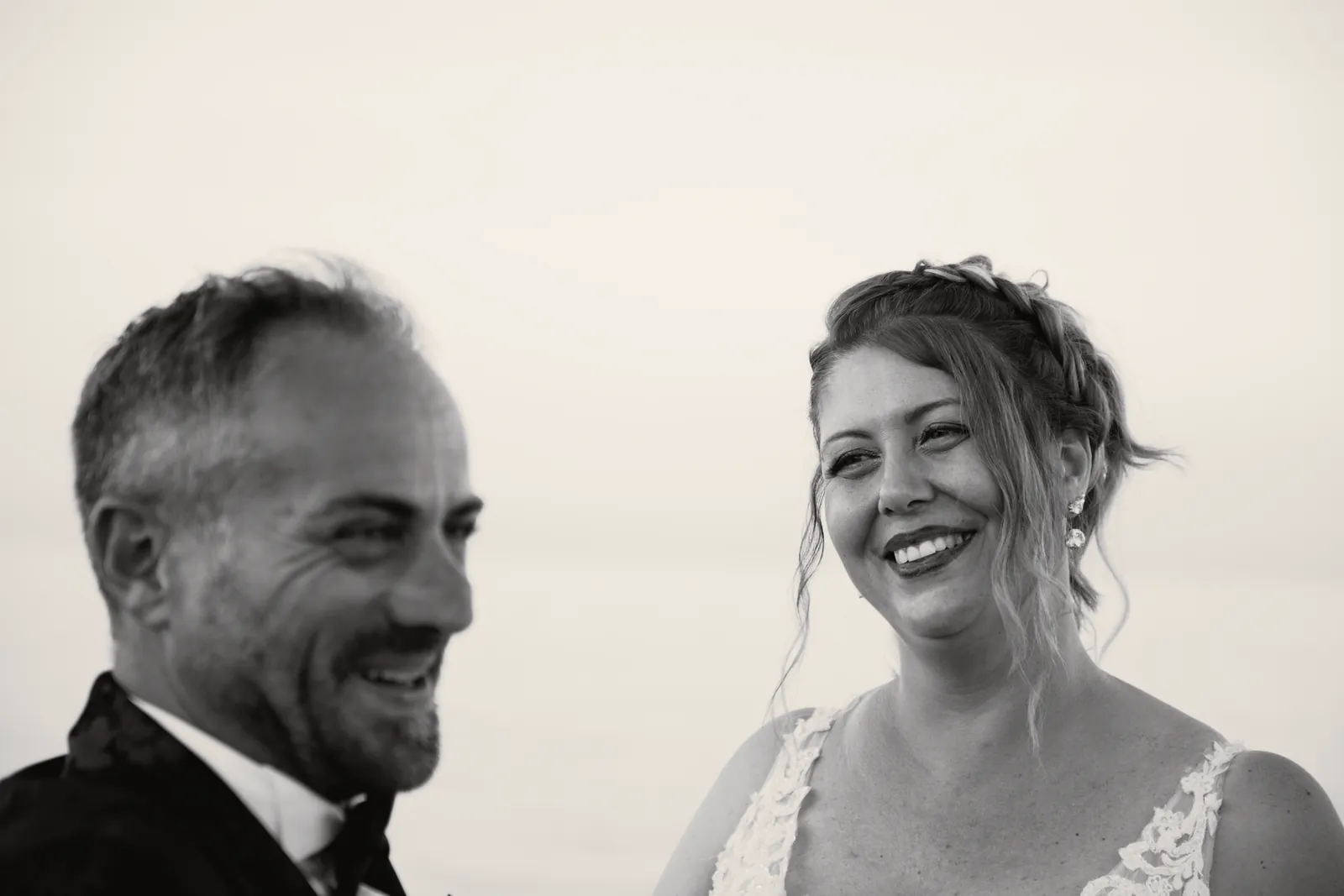 I volti degli sposi vicini che ridono, il mare sfocato alle spalle.